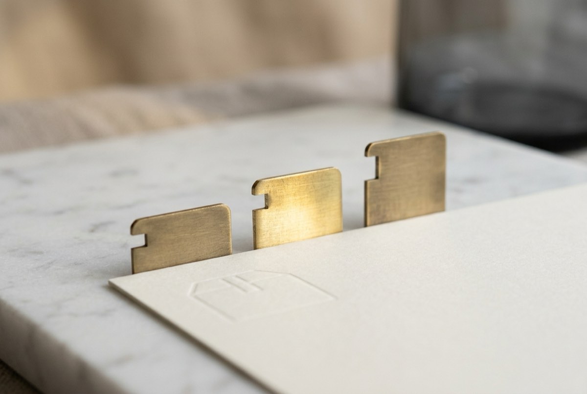 A tight macro of three brass tab dividers standing in a row on pale marble, each notched at a different height like a comparison scale, with